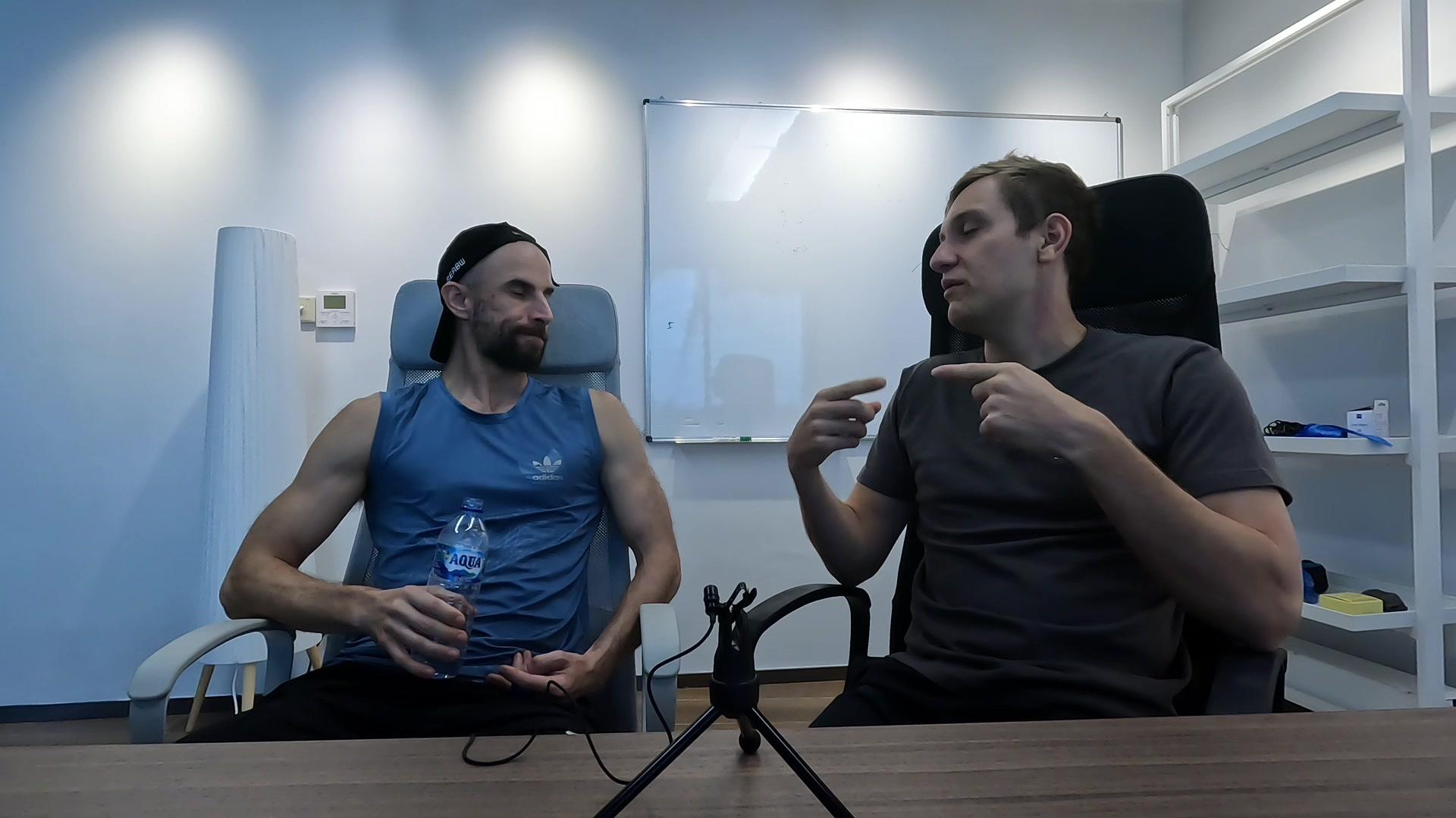 Anton Pecherkin gesturing mid-story across a table from Konrad at Network School, a whiteboard behind them